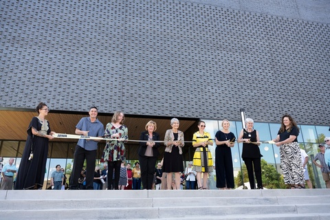 The ribbon cutting at the dedication ceremony for the new Stanley Museum of Art building. Two people hold a gold Iowa banner on each end, while 7 people pose with scissors.
