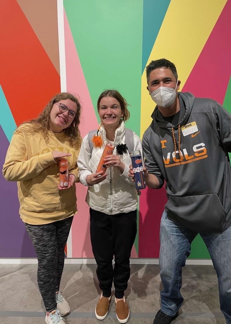 Three students stand in front of the Odita mural in the Stanley lobby, posing with the crafts they made at the October SCC event.