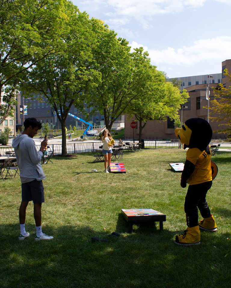 A photo of Herky playing cornhole with students on Gibson Square Park.