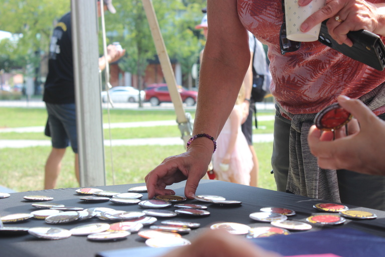 A visitor to the Stanley Museum of Art's opening weekend celebration stands in front of a black folding table in Gibson Square Park, looking through the display of pinback buttons made by the Stanley Campus Council.