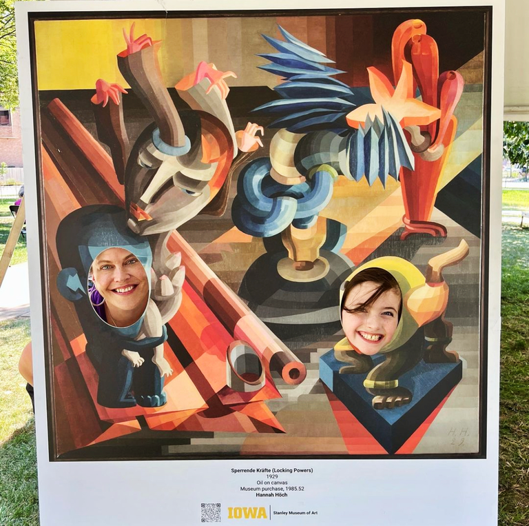 Two people pose inside a photo prop made by the SCC. The prop is a mockup of a painting in which the faces are cut out.