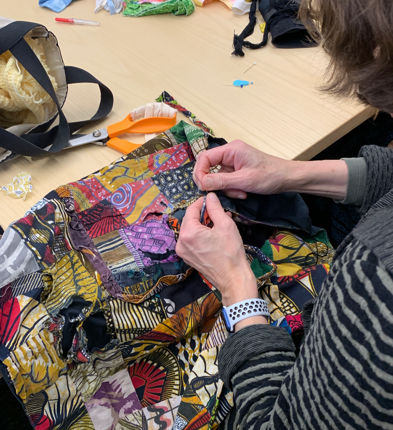 A close up image of a woman working on mending a colorful patchwork apron-style garment. 