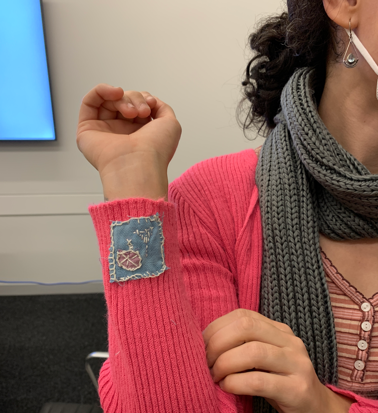 One student shows off their handiwork; they have patched the pink sweater they are wearing at the sleeve near their wrist, with a blue patch with decorative stitching.