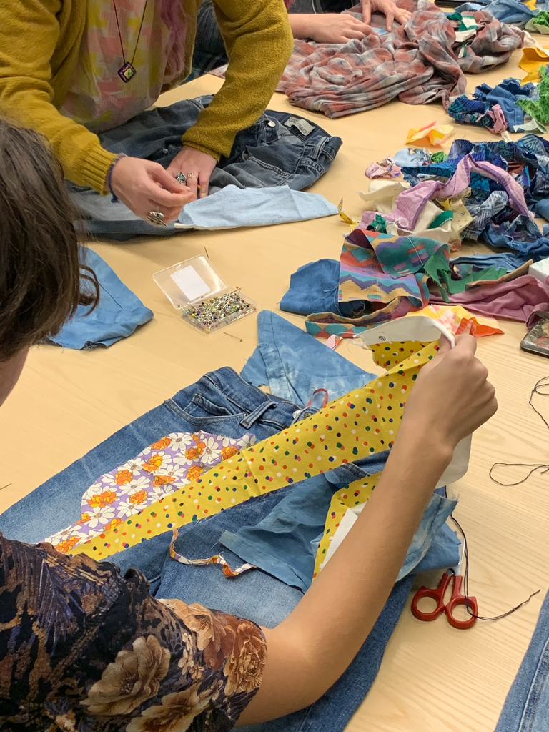 A student decides what patch fabrics they want to use for their mending project. They choose two yellow fabrics, one polka-dot and one floral, to place on their denim jeans.