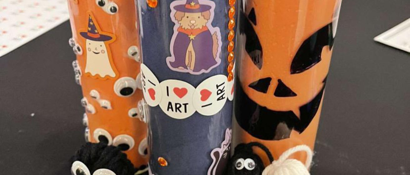 Another example of the event's crafts: Three votive candles (two orange and one purple) decorated with stickers, rhinestones, and markers, and then several pompom creatures with google eyes and other embellishments.