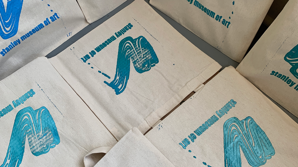 Eight tote bags fill the photograph--they are laid out along the floor to dry, all in different but similar shades and mixes of blue, green, and turquoise.